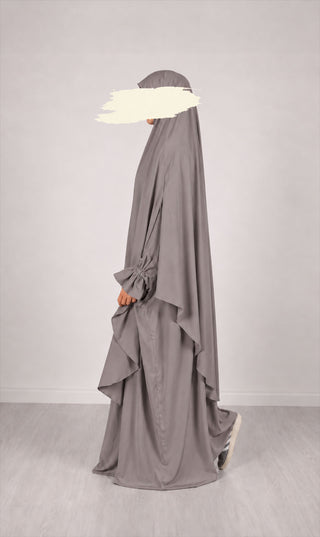 Grijze lange khimar met laagjes en asymmetrische zoom; rug zichtbaar