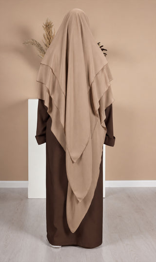 Zandkleurige khimar met asymmetrische drapering en donkerbruine lange rok eronder