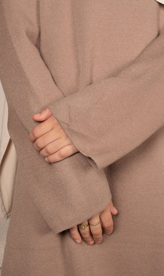 Detail van taupekleurige gebreide tuniek en wijde broek met hand bij de zoom.