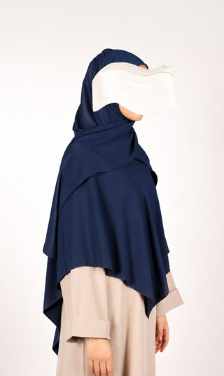 Donkerblauwe khimar-hijab met capuchon en draperende overlay; beige mouwen zichtbaar.
