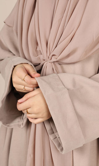 Taupekleurige abaya met strik in de taille; close-up van handen en mouwboord